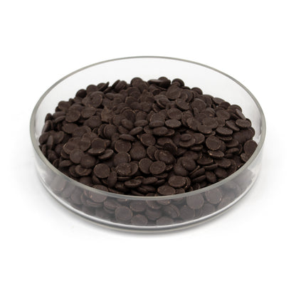 Dark brown chocolate chips piled in a clear glass bowl on a white background.