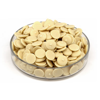 A pile of small round cream-colored chocolate wafers displayed in a clear glass bowl on a white background.