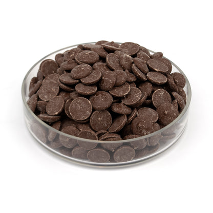 A pile of dark chocolate wafers in a glass bowl photographed on a white background