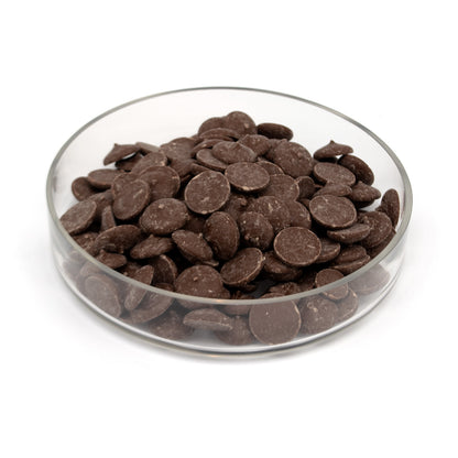 A pile of dark chocolate wafers in a glass bowl photographed on a white background