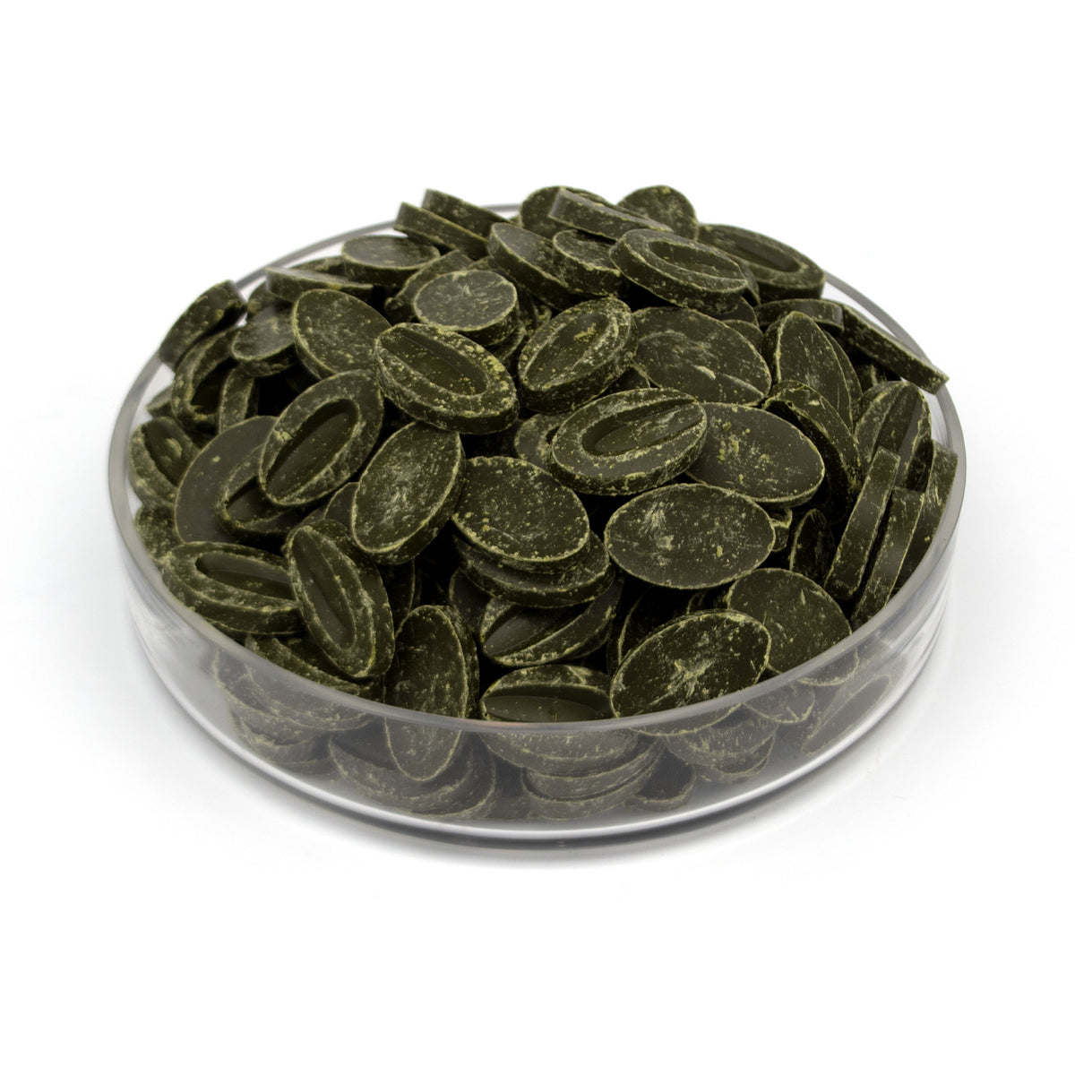 Dark olive green oval chocolate feves piled in a clear glass bowl on a white background.
