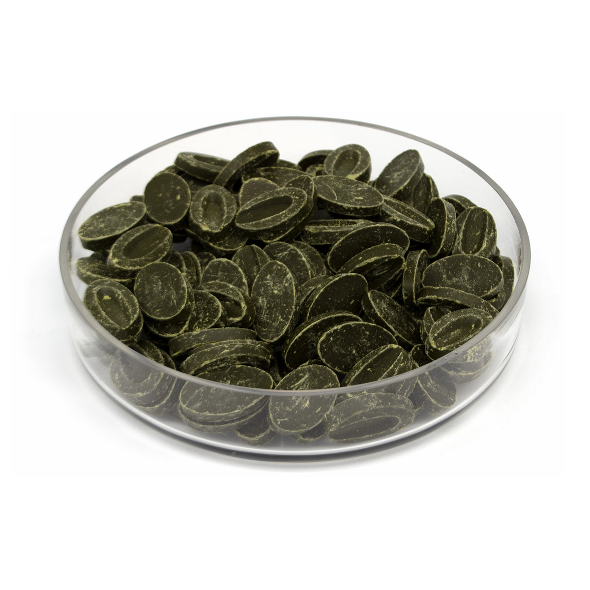 Dark green oval-shaped chocolate feves piled in a clear glass bowl on a white background.