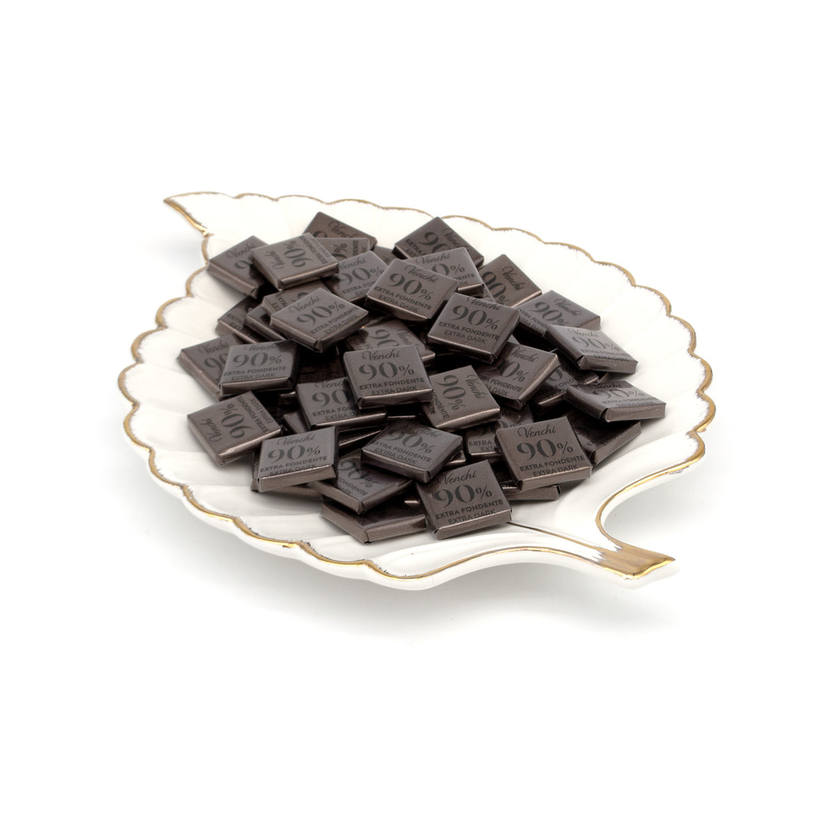 Dark chocolate pieces embossed with '90%' stacked on a white ceramic leaf-shaped plate with gold trim, set against a clean white background.